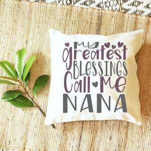 May include: White throw pillow with the text "My greatest blessings call me Nana" in purple and gray lettering with small hearts.
