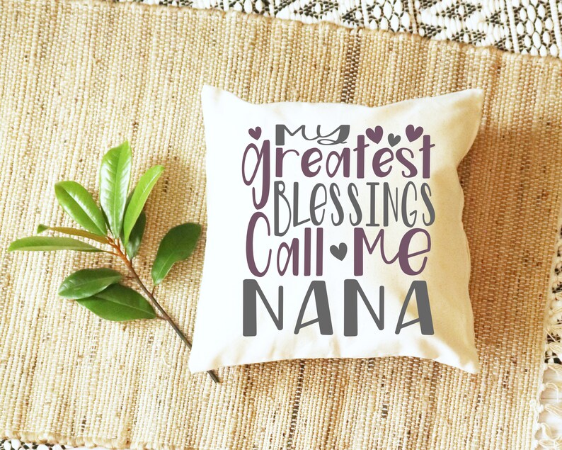 May include: White throw pillow with the text "My greatest blessings call me Nana" in purple and gray lettering with small hearts.