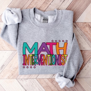 May include: Gray sweatshirt with the text "MATH INTERVENTIONIST" in colorful letters.