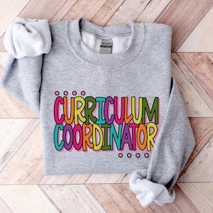 May include: Gray sweatshirt with the text "CURRICULUM COORDINATOR" in colorful letters.
