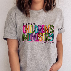 May include: A gray t-shirt with the text "CHILDREN'S MINISTRY" in colorful letters. The letters are outlined in black and have a playful, hand-drawn style.
