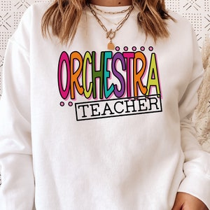 May include: White sweatshirt with the text "ORCHESTRA TEACHER" in colorful, outlined letters.