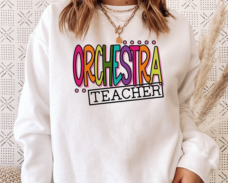 May include: White sweatshirt with the text "ORCHESTRA TEACHER" in colorful, outlined letters.