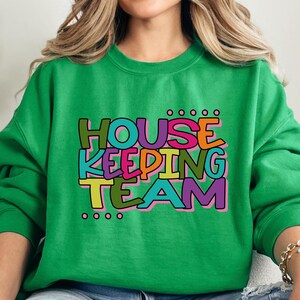 May include: Green sweatshirt with the text "HOUSEKEEPING TEAM" in colourful letters.