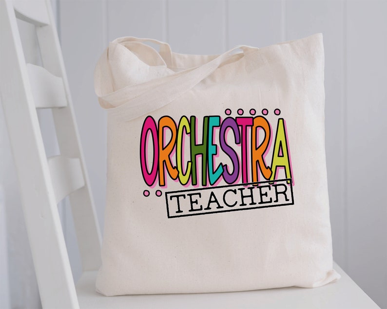 May include: A white canvas tote bag with the words "ORCHESTRA TEACHER" in colorful letters. The word "ORCHESTRA" is in a rainbow of colors and the word "TEACHER" is in a black rectangle.