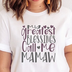 Peut inclure: T-shirt blanc avec un graphique violet et gris qui dit "Mes plus grandes b&eacute;n&eacute;dictions m'appellent Mamaw".