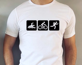 May include: White t-shirt featuring three black square icons representing triathlon events: swimming, cycling, and running. The icons are in a row, with a swimmer, cyclist, and runner. The shirt is plain white.