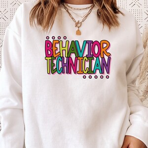 May include: White sweatshirt with the text "BEHAVIOR TECHNICIAN" in colorful letters.