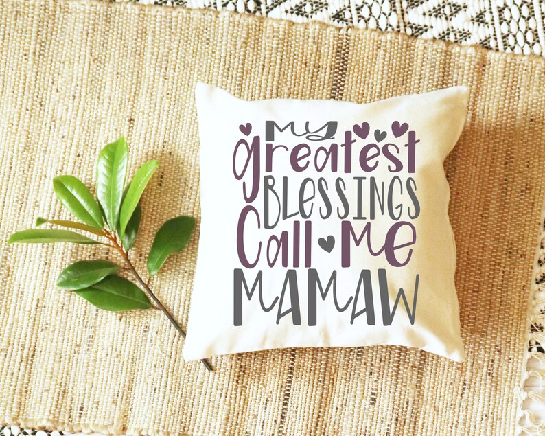 Peut inclure: Un coussin blanc avec le texte "My greatest blessings call me Mamaw" en lettres grises et violettes avec de petits c&oelig;urs.