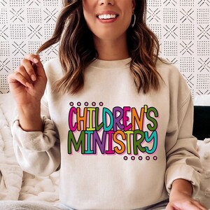 May include: A beige sweatshirt with the text "CHILDREN'S MINISTRY" in colorful, outlined letters.