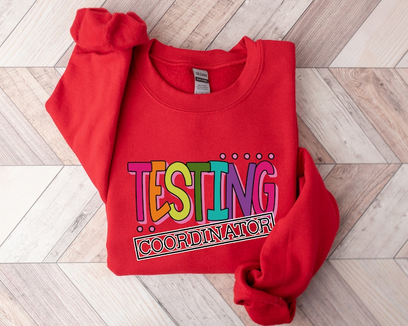 Op de afbeelding: Een felrood sweatshirt met de tekst "TESTING COORDINATOR" in kleurrijke letters. De tekst is zwart omlijnd en heeft een retro, speels ontwerp. Het sweatshirt is gemaakt van een zacht materiaal.