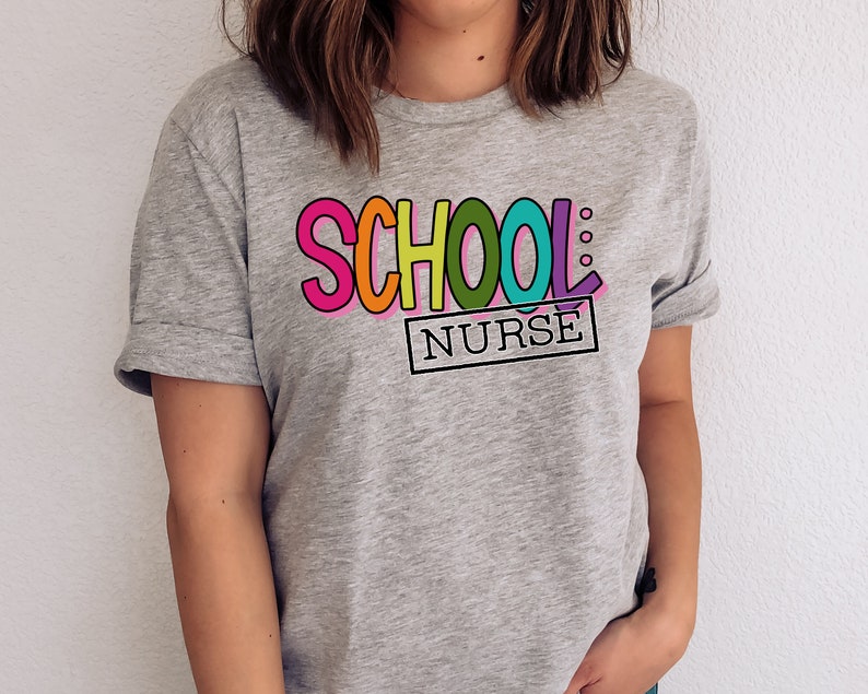 May include: A gray t-shirt with the text "SCHOOL: NURSE" in colorful letters. The letters are outlined in black and have a playful, cartoon-like style.