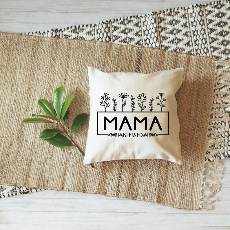 May include: A white throw pillow with black text that reads "MAMA BLESSED" and a row of black floral illustrations above the text.