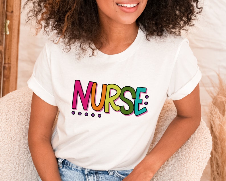 Peut inclure: T-shirt blanc avec le mot "NURSE" en lettres color&eacute;es et soulign&eacute;es. Les lettres sont dans un arc-en-ciel de couleurs avec du rose, de l'orange, du jaune, du vert et du bleu.