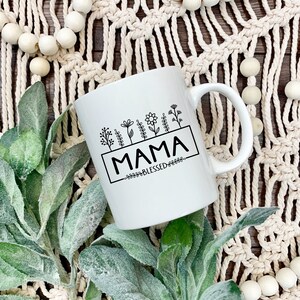 May include: White ceramic mug with a black design of flowers and the text "MAMA BLESSED".