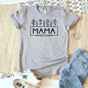 May include: A gray t-shirt with a black graphic design featuring the word "MAMA" in a box with a line of flowers above and the word "BLESSED" below.