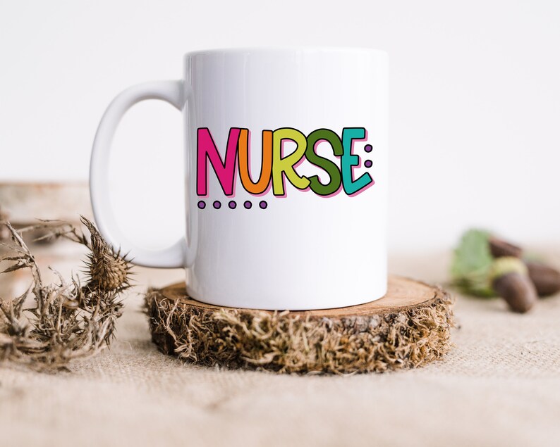 Peut inclure: Une tasse en c&eacute;ramique blanche avec un graphisme color&eacute; qui dit "NURSE:" avec quatre points violets en dessous du texte.