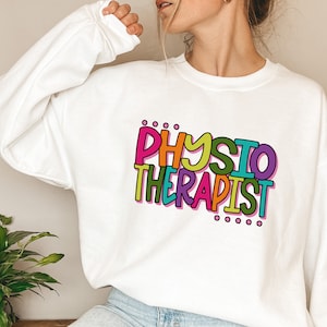 Op de afbeelding: Wit sweatshirt met een kleurrijke afbeelding met de tekst "PHYSIO THERAPIST" in een speels lettertype.