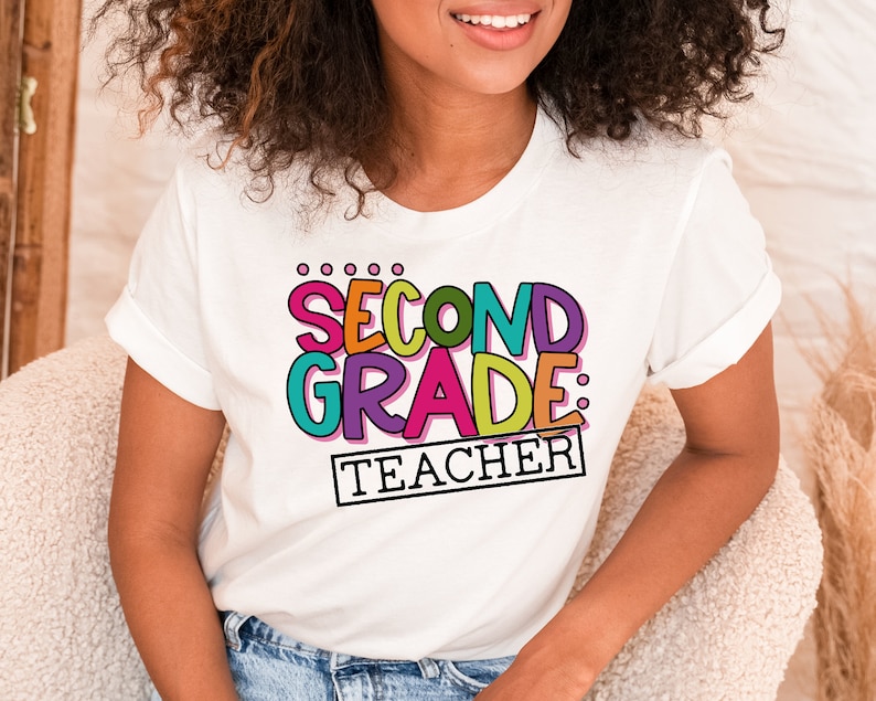 May include: White t-shirt with a colorful graphic that says "Second Grade: Teacher".