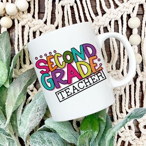 May include: White ceramic coffee mug with a colorful design that says "Second Grade Teacher".