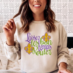 May include: A white sweatshirt with the text "Laissez les bon temps rouler" in purple and green lettering. The text is surrounded by three gold fleur-de-lis.