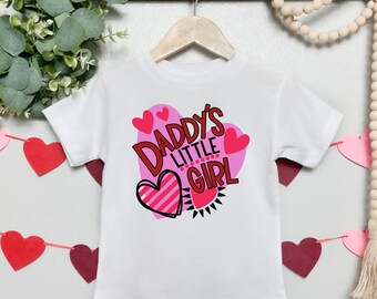 May include: White t-shirt with a pink heart design and the text "Daddy's Little Girl" in red.