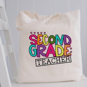 May include: A white canvas tote bag with the text "Second Grade: Teacher" in colorful letters. The letters are outlined in black and have a playful, hand-drawn style.