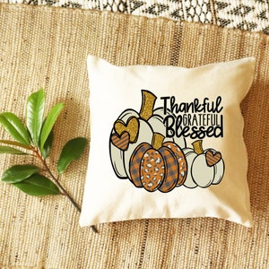 May include: A white throw pillow with a design of three pumpkins with hearts and the text "Thankful Grateful Blessed".