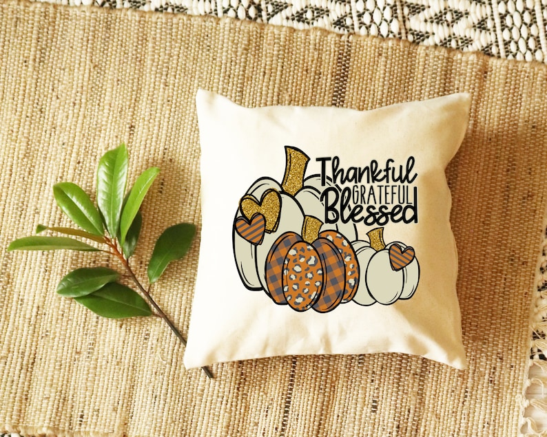 May include: A white throw pillow with a design of three pumpkins with hearts and the text "Thankful Grateful Blessed".