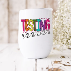 Op de afbeelding: Een witte ge&iuml;soleerde wijnbeker met een deksel. De beker heeft de woorden "TESTING COORDINATOR" in kleurrijke, vetgedrukte letters. Het ontwerp bevat roze, oranje, groene, blauwe en paarse tinten. De beker staat op een wit houten oppervlak.