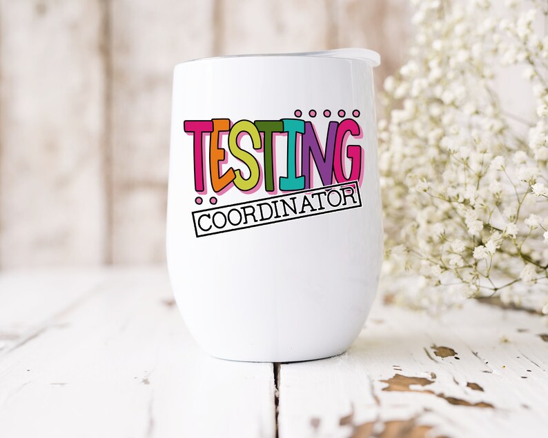 Op de afbeelding: Een witte ge&iuml;soleerde wijnbeker met een deksel. De beker heeft de woorden "TESTING COORDINATOR" in kleurrijke, vetgedrukte letters. Het ontwerp bevat roze, oranje, groene, blauwe en paarse tinten. De beker staat op een wit houten oppervlak.