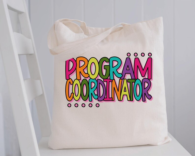 May include: A cream-colored tote bag with the words "PROGRAM COORDINATOR" in large, colorful letters. The text is outlined in black and features a rainbow of colors, including pink, orange, green, teal, purple, and yellow. The bag has two handles.