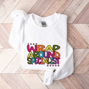 May include: White sweatshirt with the text "...WRAP AROUND SPECIALIST..." in colorful, outlined letters.
