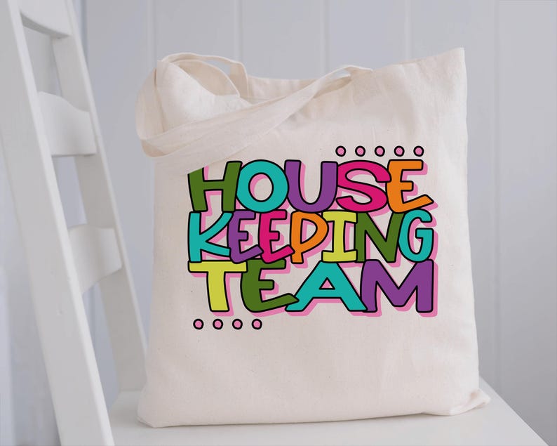 May include: A white canvas tote bag featuring the text "HOUSEKEEPING TEAM" in colourful letters. The letters are outlined in black and have a playful, hand-drawn style.