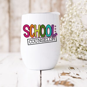以下が含まれることがあります： 白いステンレス製のタンブラーに、カラフルな「SCHOOL COUNSELOR」のデザインが施されています。タンブラーには蓋が付いており、白い木製の表面の上に置かれています。