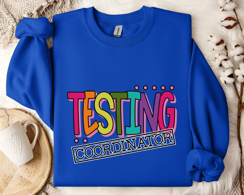 Op de afbeelding: Een koningsblauwe sweatshirt met de tekst "TESTING COORDINATOR" in een kleurrijk, retro lettertype. De tekst is zwart omlijnd en geplaatst tegen een witte achtergrond. De sweatshirt is gemaakt van een zacht materiaal.