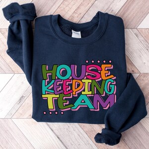 May include: A navy blue sweatshirt with the text "HOUSE KEEPING TEAM" in colourful letters. The letters are outlined in white and have a dotted pattern around them.