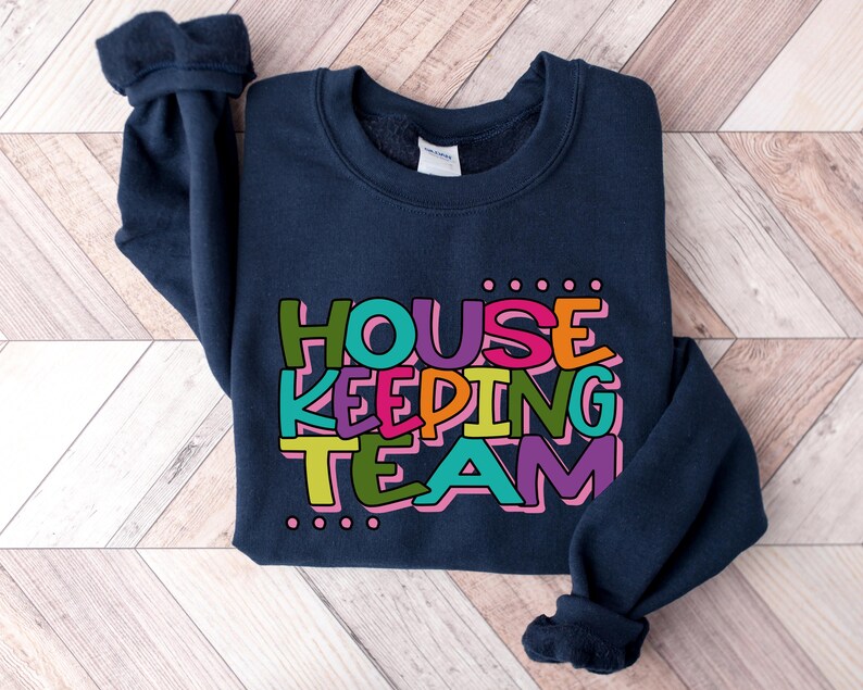 May include: A navy blue sweatshirt with the text "HOUSE KEEPING TEAM" in colourful letters. The letters are outlined in white and have a dotted pattern around them.