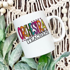 May include: White ceramic mug with a colorful graphic that says "ORCHESTRA TEACHER".