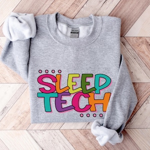 May include: Grey sweatshirt with the text "SLEEP TECH" in colourful, outlined letters. The letters are in different colours, including pink, green, yellow, and blue.