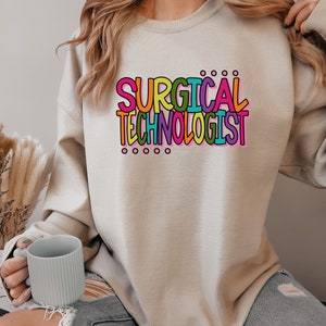 May include: A light beige sweatshirt with the text "SURGICAL TECHNOLOGIST" in colorful letters.