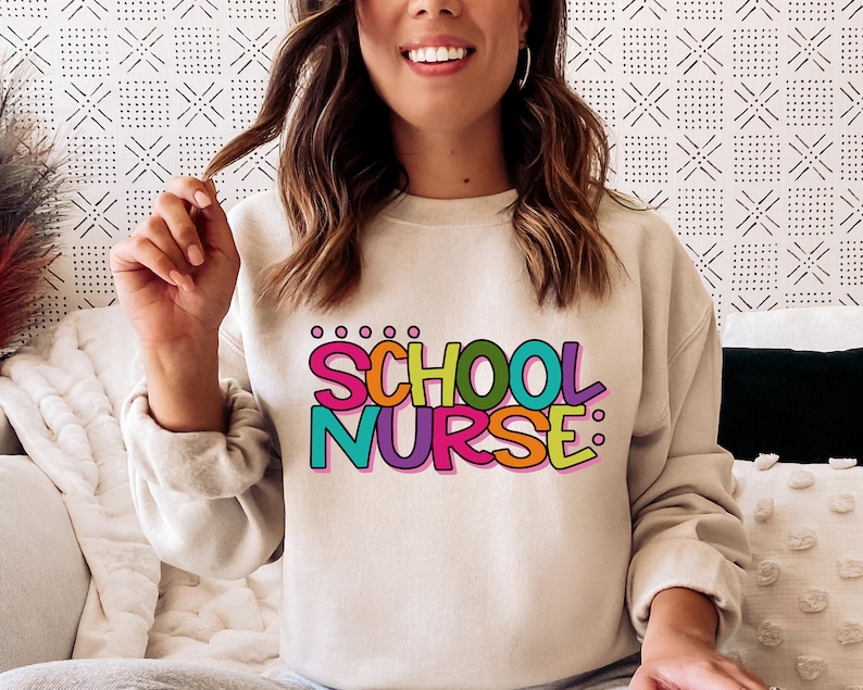 May include: A light beige sweatshirt with the text "SCHOOL NURSE" in colorful, outlined letters.