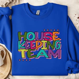 May include: A royal blue sweatshirt with the text "HOUSE KEEPING TEAM" in colourful, playful lettering.