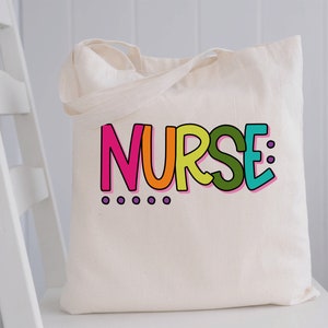 Peut inclure: Un sac fourre-tout en toile blanche avec le mot "NURSE" imprim&eacute; en lettres color&eacute;es. Les lettres sont soulign&eacute;es de noir et ont un sch&eacute;ma de couleurs arc-en-ciel. Il y a six points violets sous le mot.