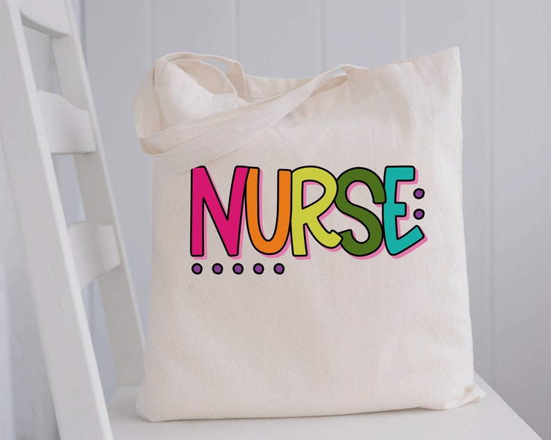 Peut inclure: Un sac fourre-tout en toile blanche avec le mot "NURSE" imprim&eacute; en lettres color&eacute;es. Les lettres sont soulign&eacute;es de noir et ont un sch&eacute;ma de couleurs arc-en-ciel. Il y a six points violets sous le mot.