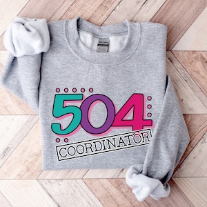 May include: Gray sweatshirt with a graphic design of the number 504 in teal, purple, and pink with the text "COORDINATOR" in a black box.