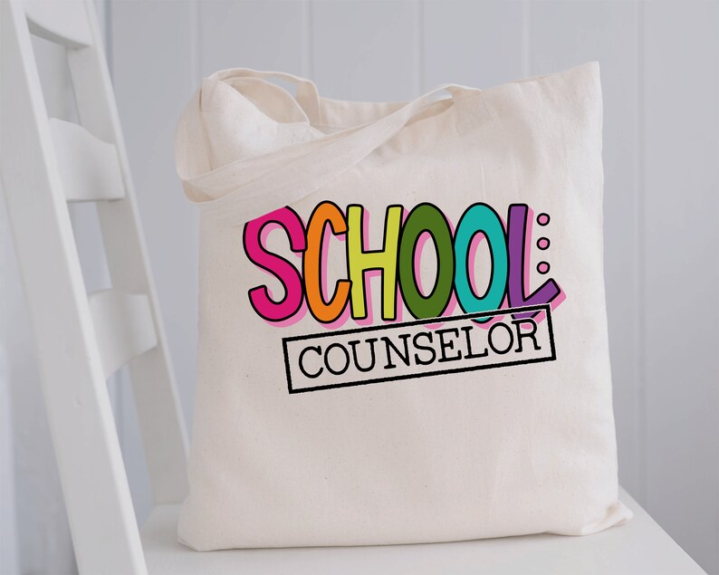 以下が含まれることがあります： 白地のキャンバス地のトートバッグに、「SCHOOL COUNSELOR」という文字が黒で印刷されています。「SCHOOL」という文字は虹色です。
