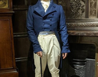Op de afbeelding: Een man in een blauwe jas met een witte stropdas en witte broek. Hij houdt een zwarte wandelstok vast en staat voor een open haard.