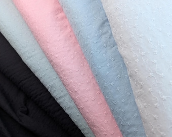 May include: A collection of pastel-colored fabrics, including black, light blue, pink, and white. Each fabric is delicately embroidered with a floral pattern, creating a textured surface. The fabrics are arranged in a diagonal composition, showcasing their colors and textures.