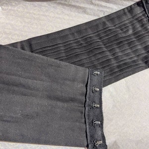 May include: Black fabric corset with adjustable straps and multiple hooks. The corset is made of a smooth, soft fabric and has a pleated design.
